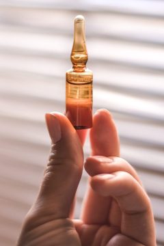 A closeup of a person holding an ampoule under the sunlight with a window on a blurry background